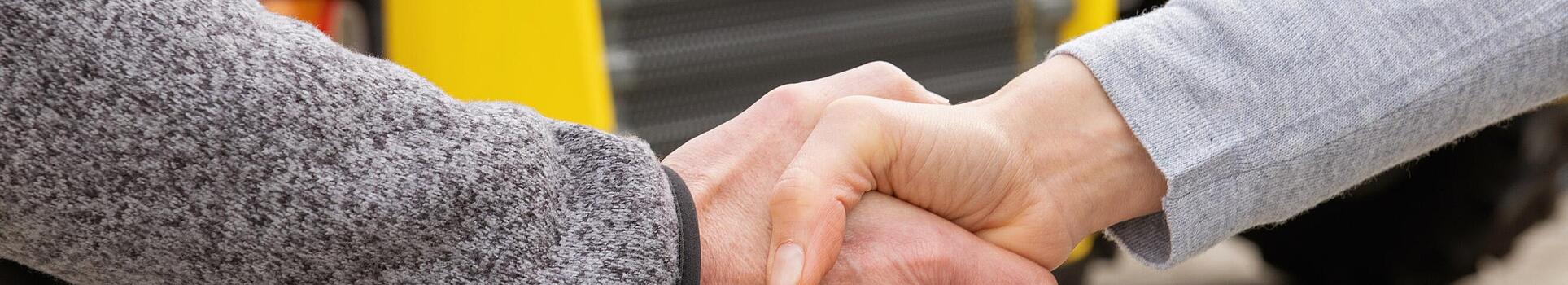 Handshake between Wacker Neuson employee and customer, Wacker Neuson construction machines in background.