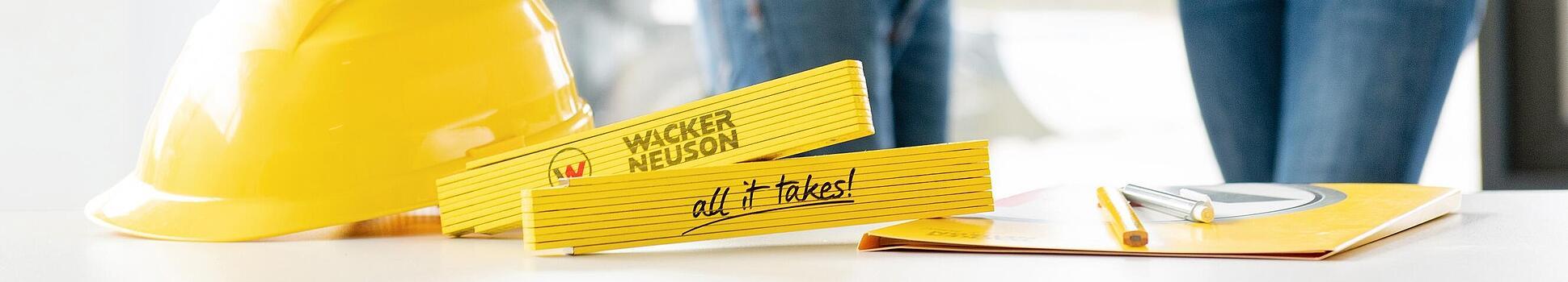 Wacker Neuson merchandise items lying on table in foreground, Wacker Neuson employees in background.