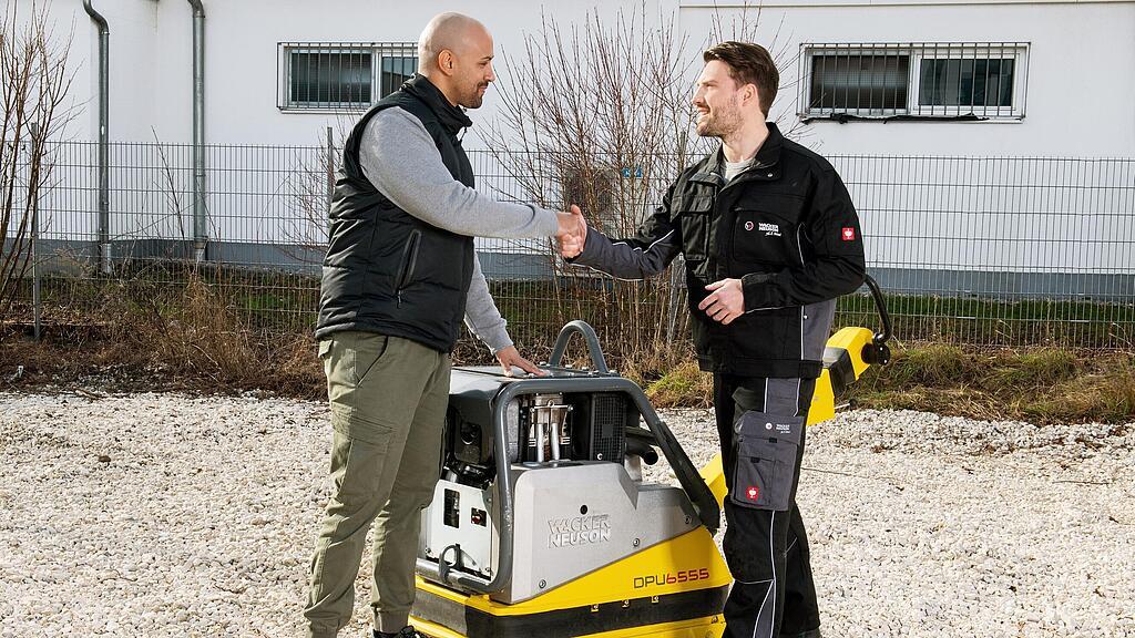Wacker Neuson Mitarbeiter gibt Kunden die Hand vor einer Wacker Neuson Vibrationsplatte.