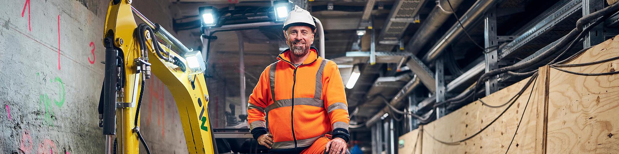 man standing in front of electric excavavtor at construction site