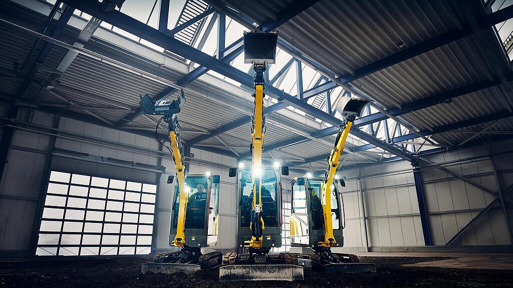 Drei Wacker Neuson Minibagger mit angehobenen Auslegern in Industriehalle