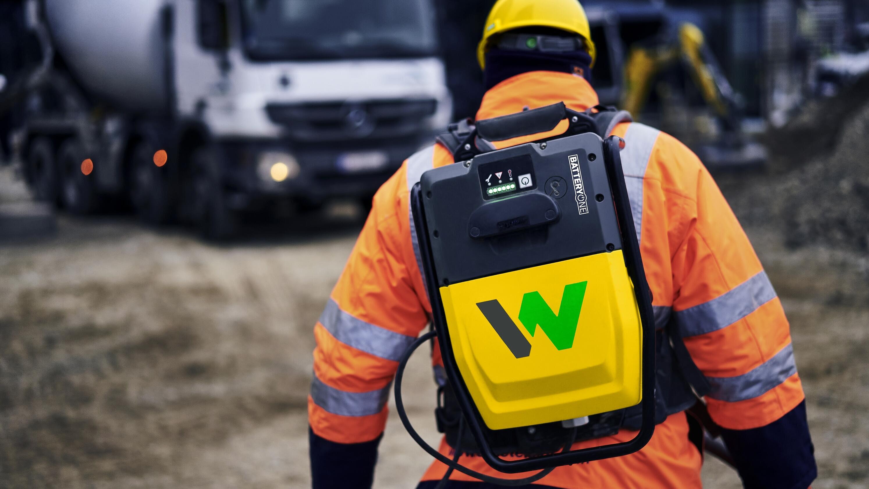 Il lavoratore edile trasporta lo zaino  convertitore batteria ACBe di Wacker Neuson in un cantiere edile.